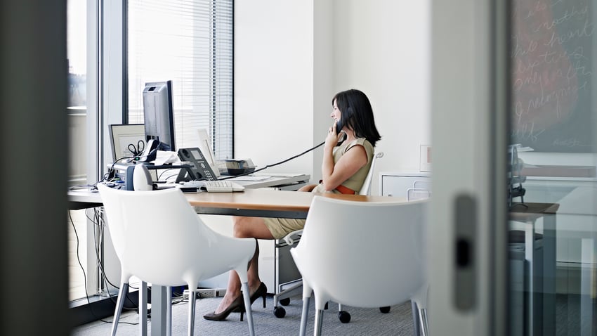 Businesswoman sitting at desk in office talking on phone smiling