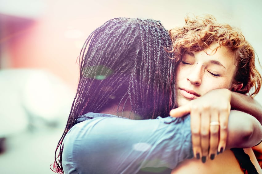 Mujer africana abrazando a su novia blanca al aire libre.