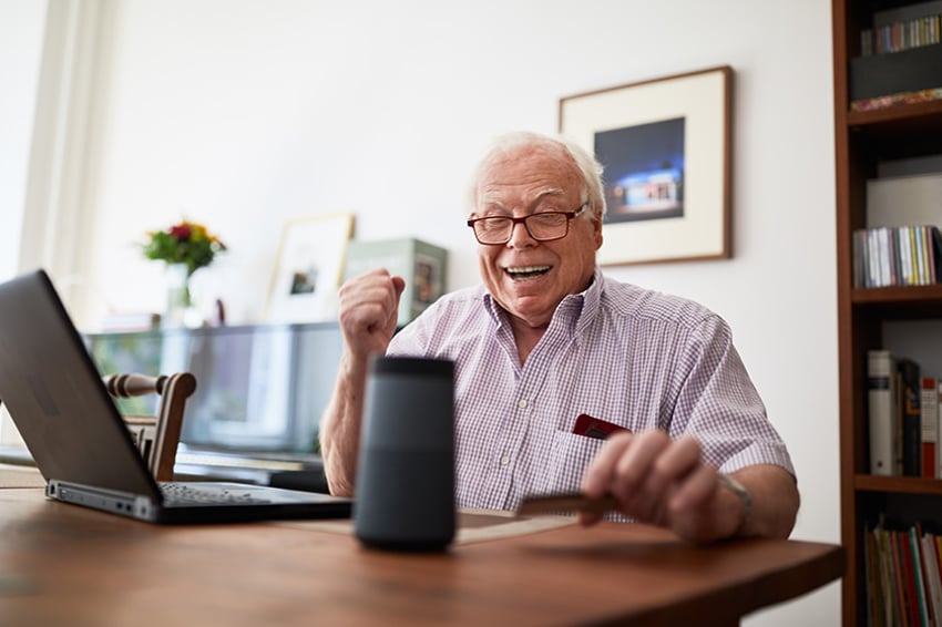 Hombre mayor comprando online con una tarjeta de crédito, un portátil y un dispositivo de altavoz inteligente.