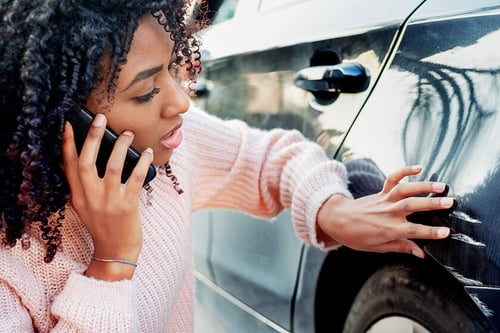 woman on cell phone examining scratches on car