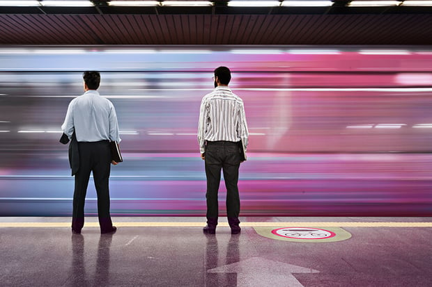 two men standing on platform while train rushes past